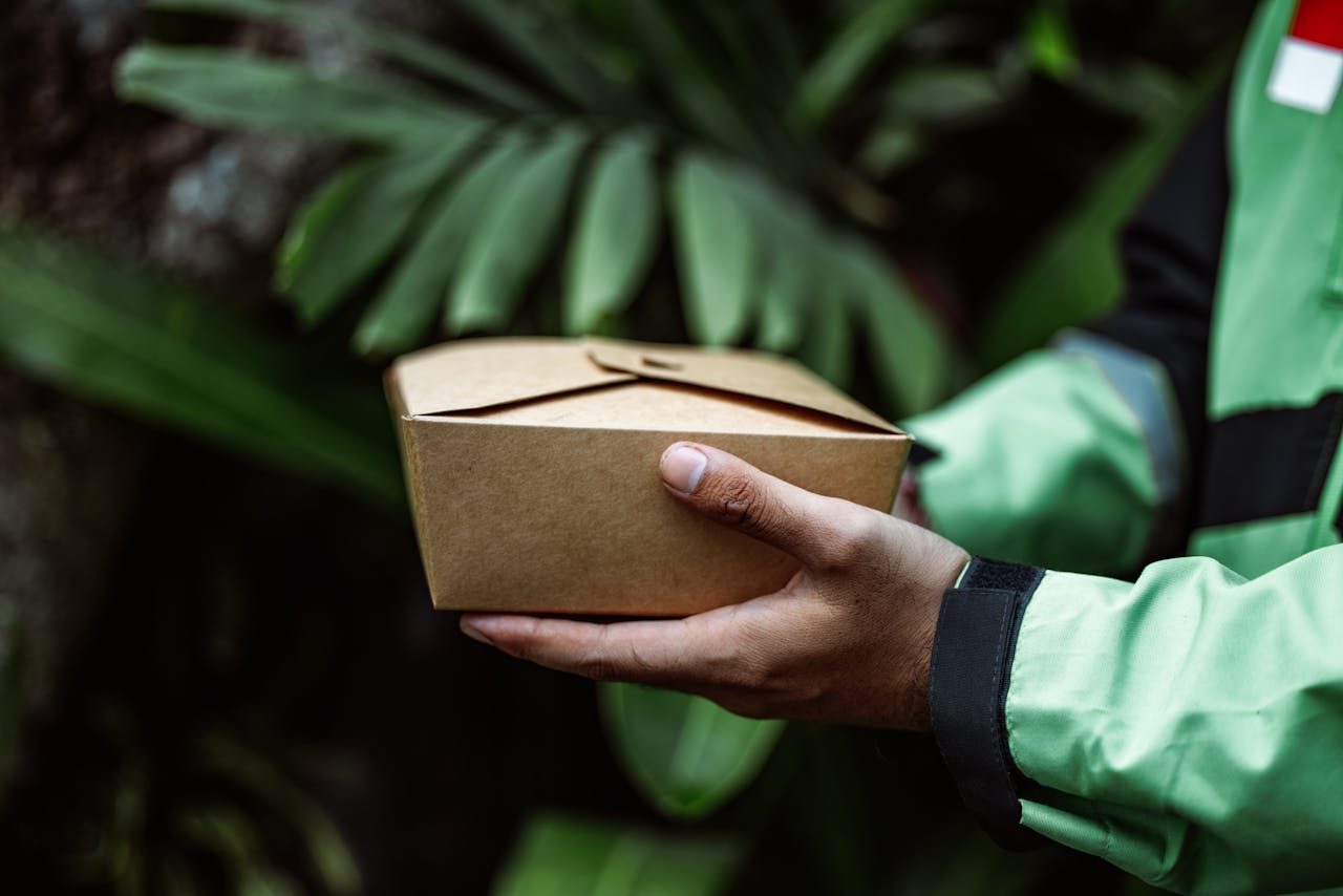 Hands holding an eco-friendly cardboard food box outdoors. Sustainable delivery concept.