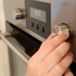 Close-up of hands adjusting the temperature dial on a modern kitchen oven.
