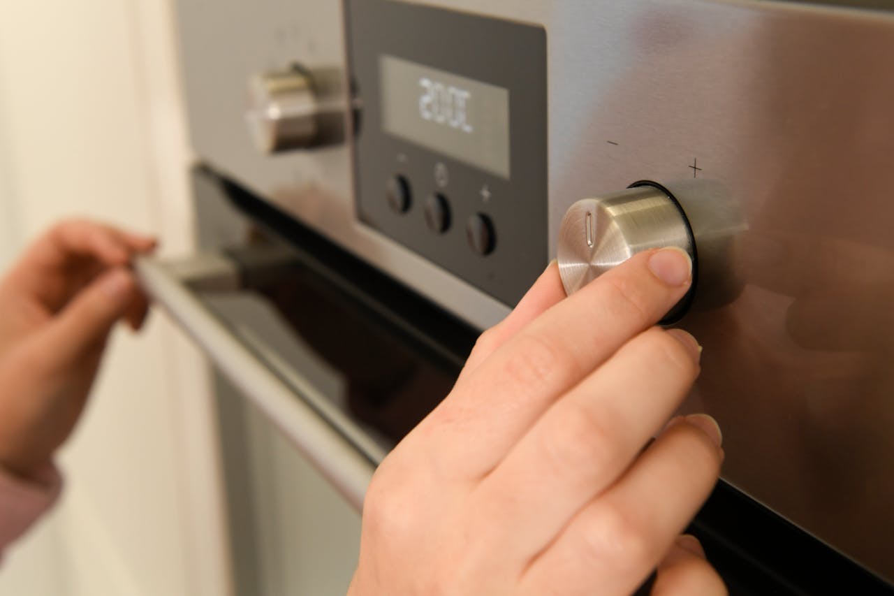 Close-up of hands adjusting the temperature dial on a modern kitchen oven.